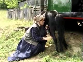 Country girl with red hair in simple attire engages in oral activity with a horse outside